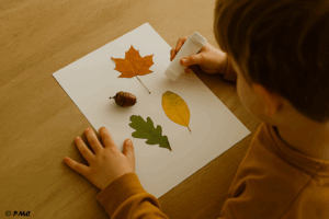 Enfant collant des feuilles et un gland sur une feuille blanche, réalisant une création simple avec des éléments naturels.
