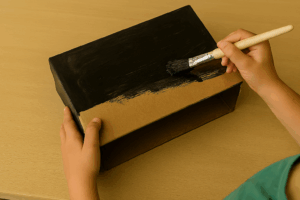 Mains d’un enfant peignant une boîte en carton en noir pour un bricolage Halloween