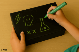 Enfant dessinant des symboles d’Halloween sur une boîte noire avec un feutre vert
