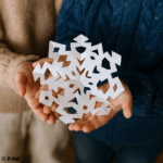 Main d’un enfant tenant un flocon en papier fraîchement déplié, aux motifs géométriques
