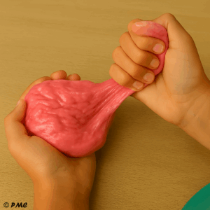 Préparation d’un slime rose nacré avec les ingrédients posés sur une table et la main d’un enfant versant du liquide