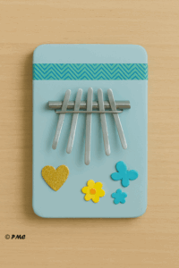 Kalimba artisanale fabriquée avec une boîte plate et des tiges métalliques, décorée avec des éléments colorés.