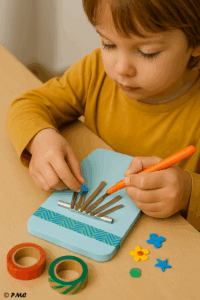 Enfant décorant une kalimba artisanale avec des gommettes et un feutre orange.