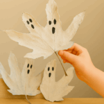 Feuilles peintes en fantômes suspendues à des branches pour un bricolage d’Halloween fait par un enfant