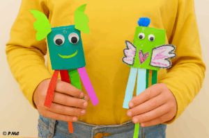 Trois marionnettes colorées faites par des enfants avec des rouleaux de carton, du papier crépon et des décorations fantaisistes.