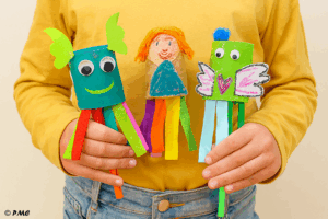 Trois marionnettes colorées faites par des enfants avec des rouleaux de carton, du papier crépon et des décorations fantaisistes.