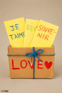 Boîte en carton décorée par un enfant, remplie de papiers pliés avec des mots tendres écrits à la main