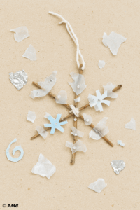 Flocon suspendu fait main par un enfant avec bâtonnets noués, papier aluminium, perles et sucre