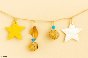 Décorations de Noël enfantines accrochées dans le sapin : étoile froissée, pomme de pin peinte, boule en papier et feuille séchée