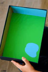 Boîte à chaussures décorée avec du papier vert pour l’herbe et du papier bleu pour le ciel, étape de préparation du fond du jardin des fées.