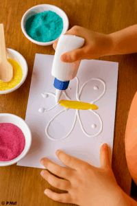 Main d’enfant appliquant de la colle sur le dessin d’une tortue pour préparer le collage du sable.