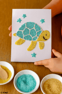 ableau sensoriel représentant une tortue réalisée avec du sable turquoise, du sel blanc et de la semoule jaune.