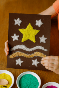 Tableau noir décoré de sable doré et blanc représentant une étoile centrale entourée de motifs festifs.