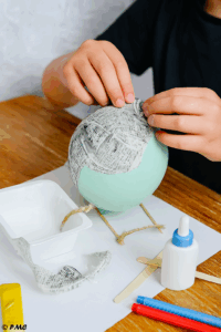 Mains d’enfant recouvrant un ballon de papier journal pour créer la voile en papier mâché