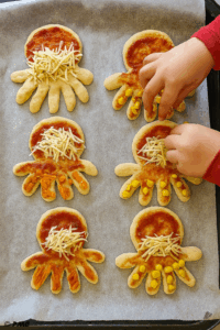 Mini pizzas pieuvres cuites présentées dans une assiette avec main d’enfant