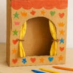 théâtre en carton décoré, avec rideaux dorés, frise rouge et marionnettes représentant différentes émotions.