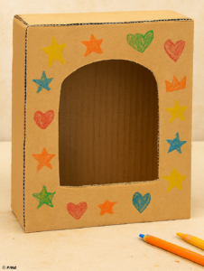 Photo d’une boîte en carton avec une grande fenêtre arrondie découpée sur sa face avant, posée sur une table.